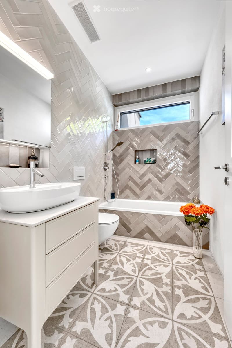 Contemporary bathroom with herringbone wall tiles, floating vanity, under-mount sink, shower with ceiling-mounted showerhead, and bathtub with niche shelves.