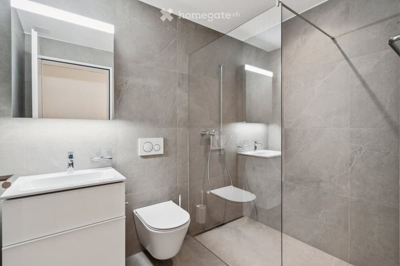 Modern bathroom with grey marble tiles, white fixtures, a glass-enclosed shower, and built-in storage.