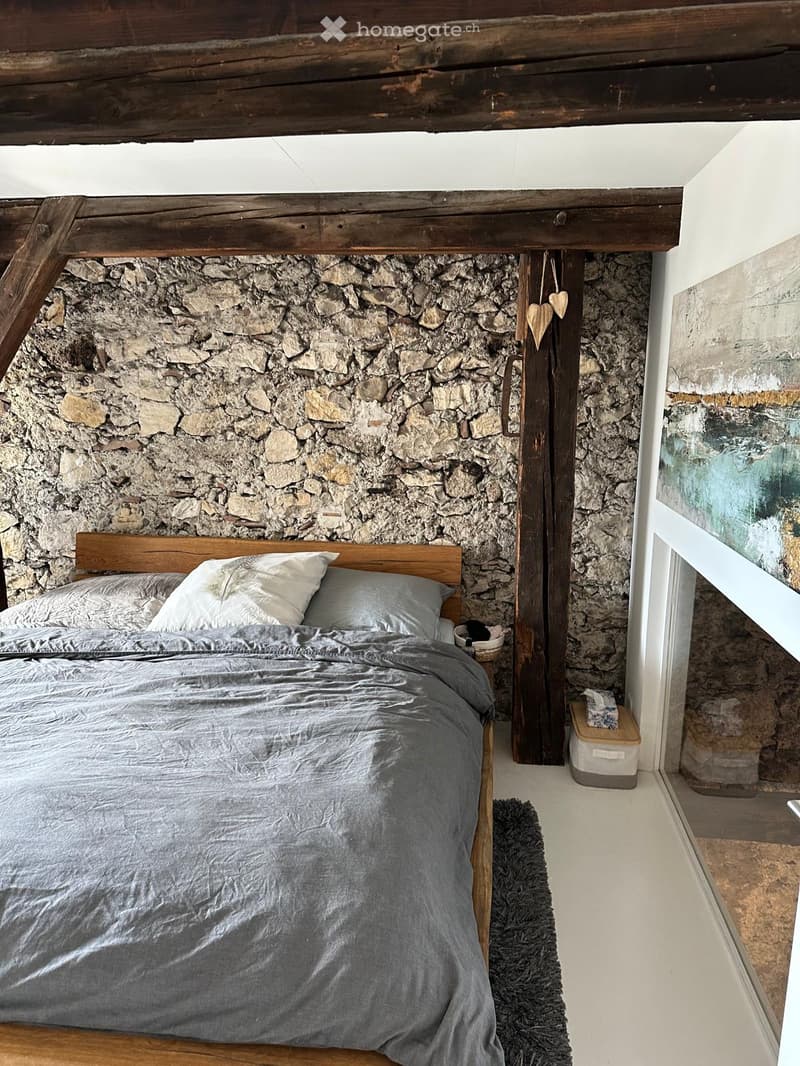 Cozy bedroom with a wooden bed, stone accent wall, and a small nightstand with a basket on top.