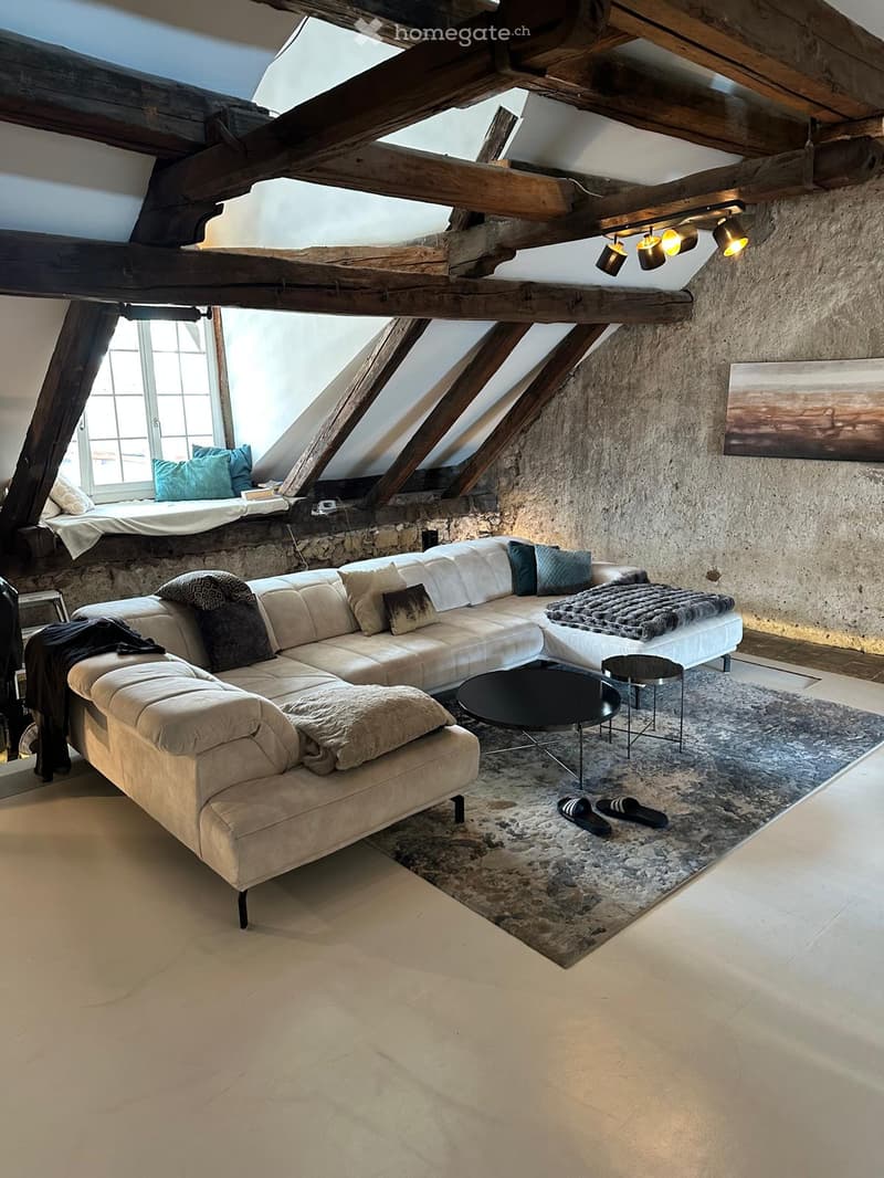 Modern living room with exposed wooden beams, a large sectional sofa, coffee table, ottoman, side table, and a painting on the wall.