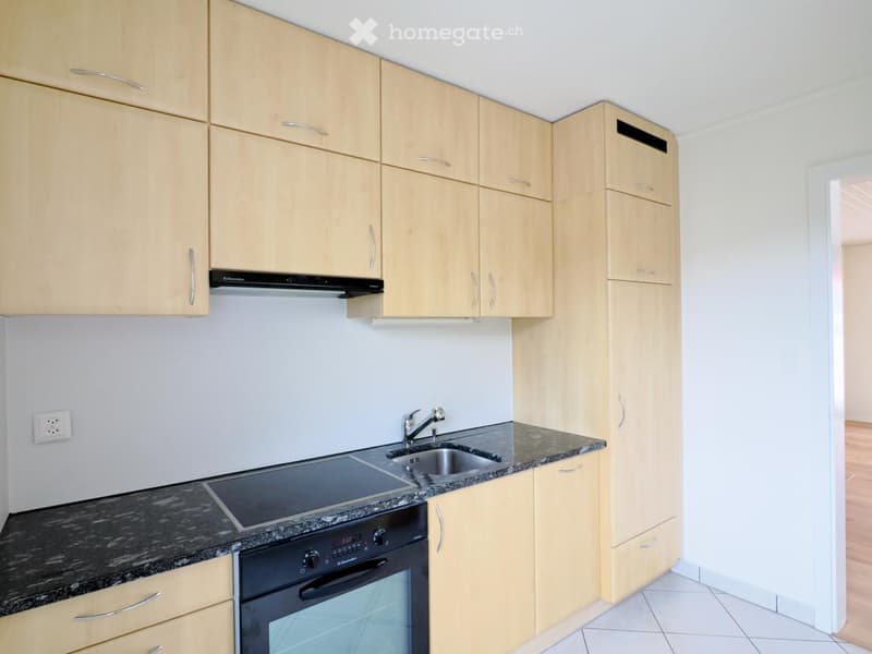 Modern kitchen with light wooden cabinets, granite countertops, stainless steel sink, and built-in appliances including an oven and induction cooktop.
