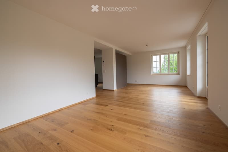Empty room with light wooden flooring and white walls, featuring a large window and several electrical outlets.