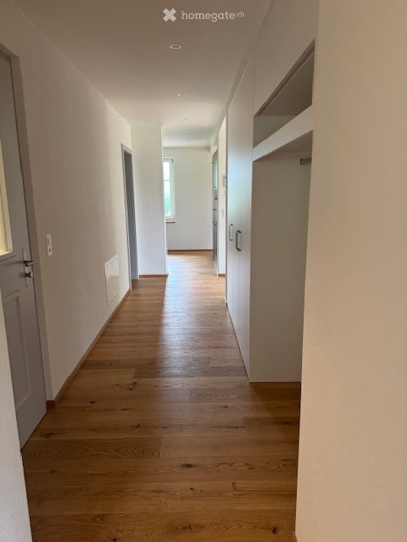 Empty hallway with wooden flooring, white walls, and several doors leading to other rooms.