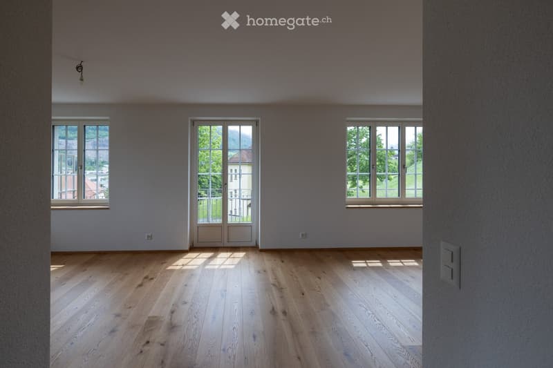 Empty room with light wooden flooring, large windows, and a door leading to a balcony.