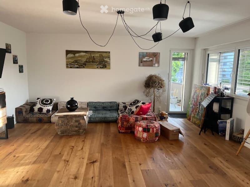 Living room with wooden flooring, a sofa, coffee table, ottoman, and decorative items including a vase and picture frames.