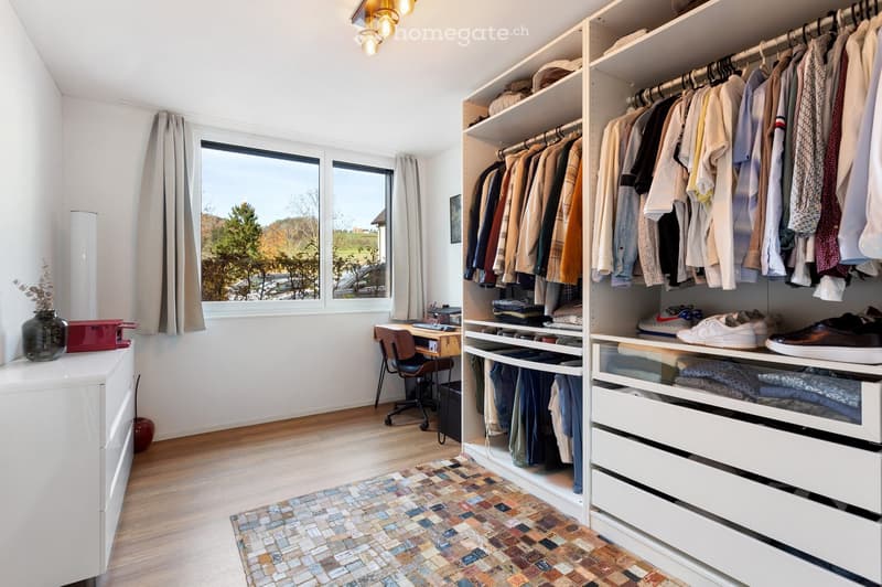 A well-organized walk-in closet with built-in wardrobe, shelves, and drawers. Features a wooden desk, chair, and decorative vase on a side table.