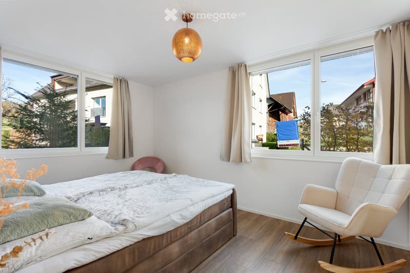 Bright bedroom with large windows, a neatly made bed, a rocking chair, and a decorative lamp hanging from the ceiling.