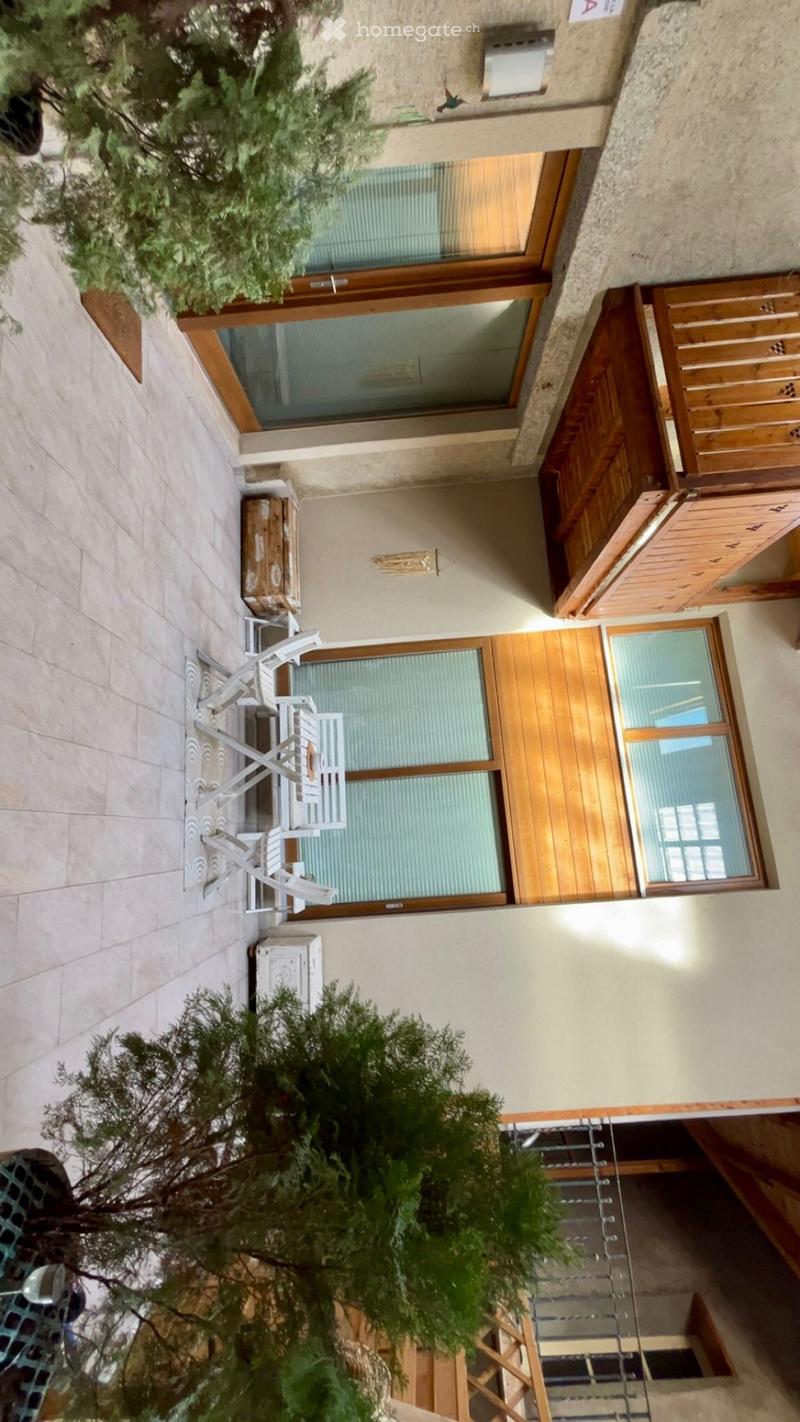Balcony with wooden railings, tiled floor, two white chairs, small table, and potted plants.