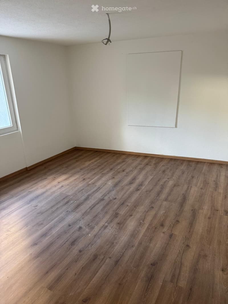 Empty room with wooden flooring and white walls, featuring a window and a blank canvas on the wall.