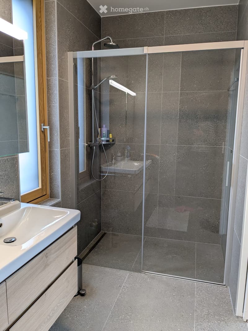 modern bathroom with glass shower, white sink, wooden cabinet, tiled floor