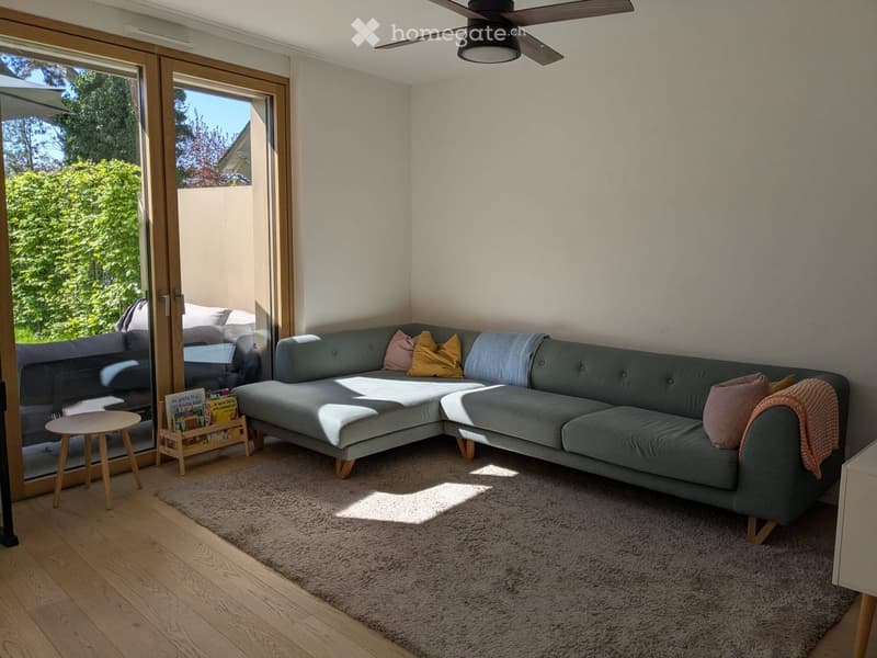 L-shaped sofa, carpet, wooden table, sliding glass doors, balcony, ceiling fan, books, pillows