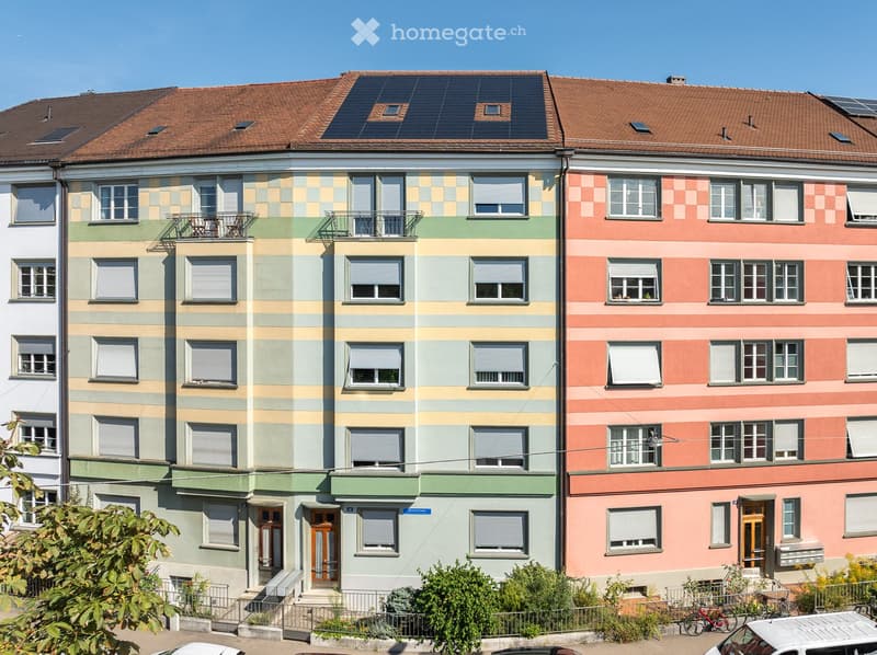 Multi-story residential building with colorful striped facade, multiple windows, balconies, and solar panels on the roof.