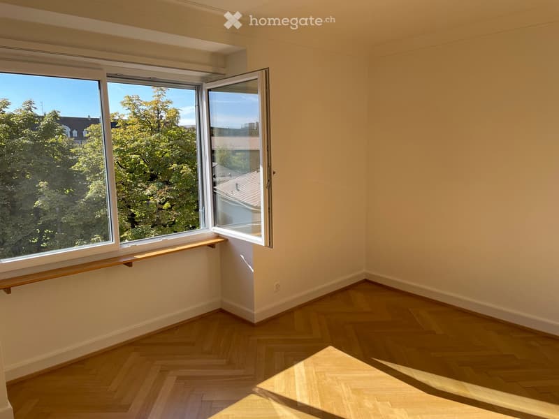 Empty room with wooden flooring, large windows, and a small wooden shelf near the window.