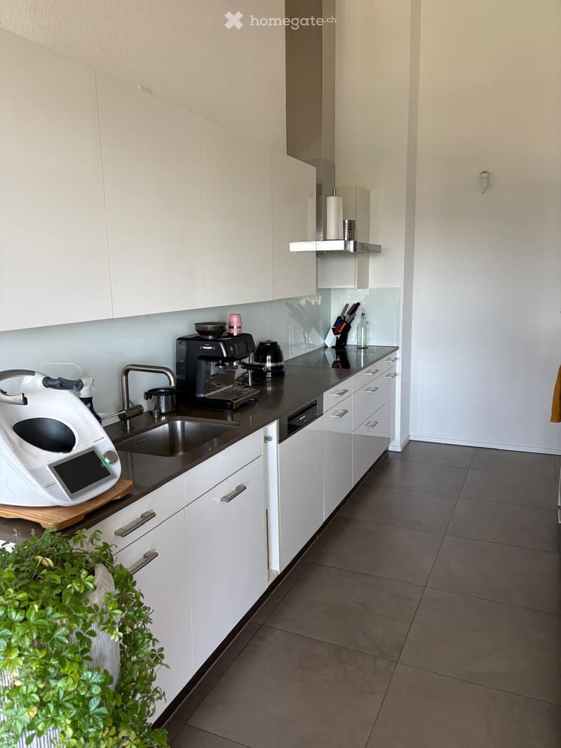 Modern kitchen with white cabinets, black countertops, stainless steel sink, coffee maker, toaster, blender, and various kitchen utensils.