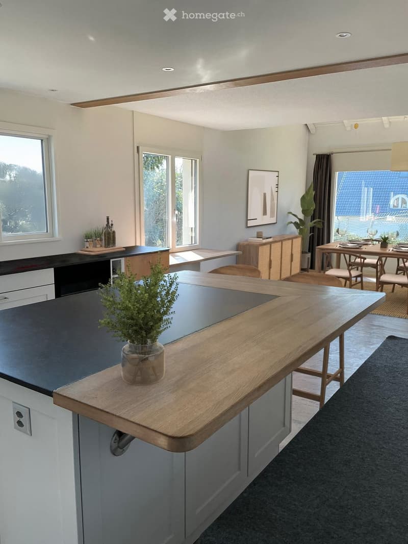 Kitchen. Modern kitchen with a wooden island, black countertop, dining area, and large windows.