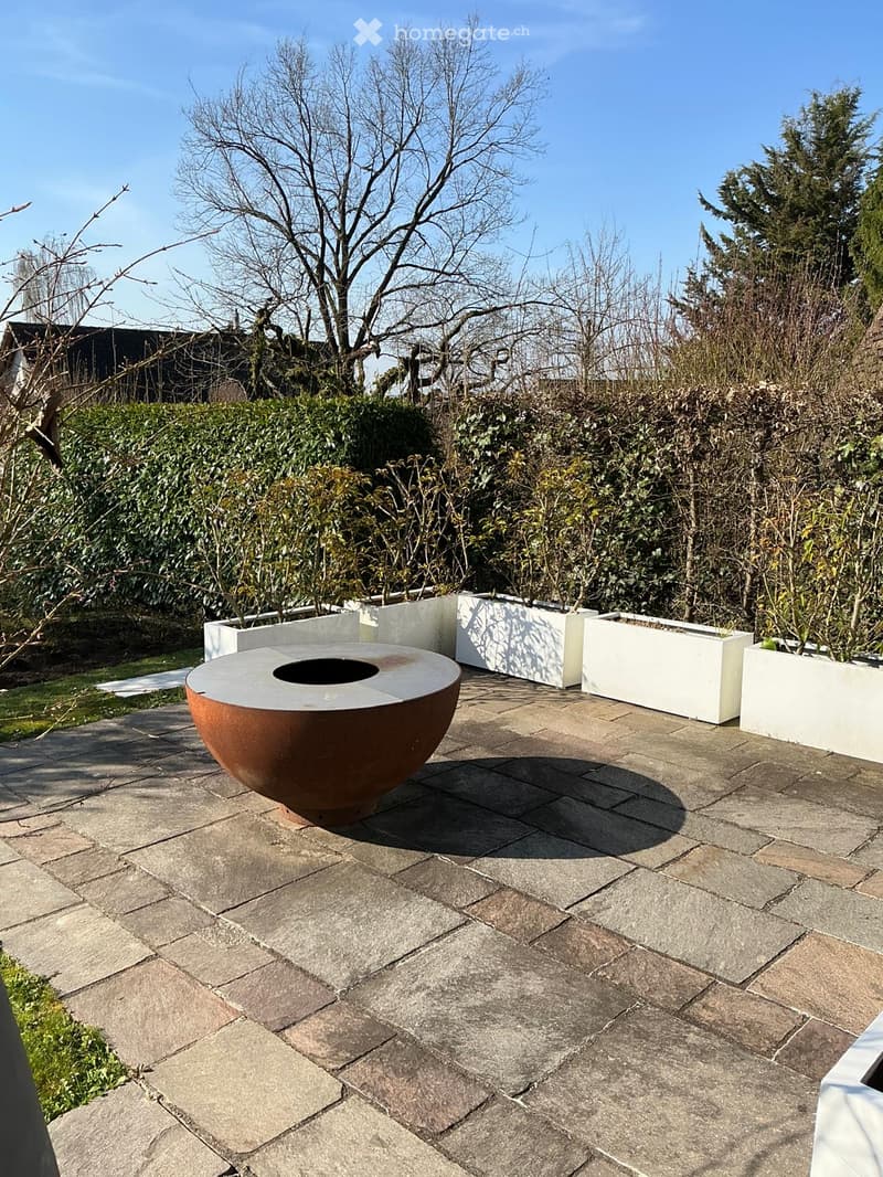 Outdoor area with a fire pit, brick floor, white planters, and a hedge in the background