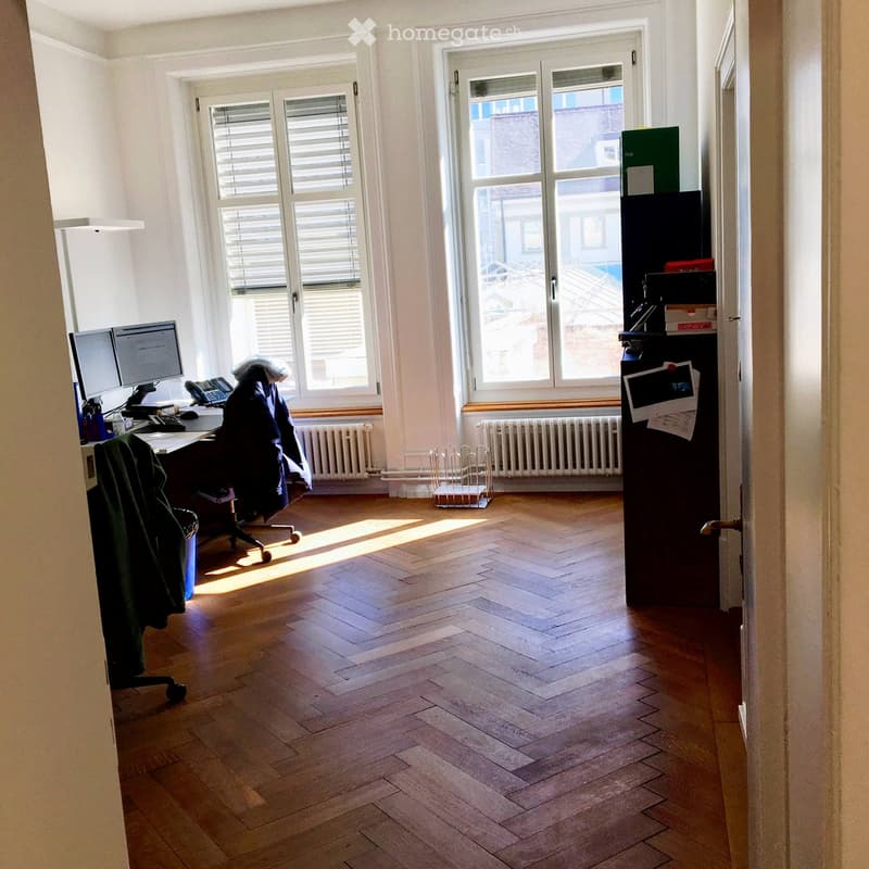 Wooden floors, office chair, desk, 2 computer monitors, radiators, sunlit, cabinets, door