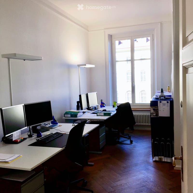 Two desks, three monitors, office chairs, small lamps, printer, radiator.