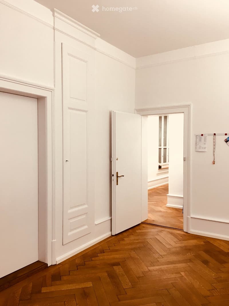 Empty room with two white doors, wooden floor, two small white window openings on right side