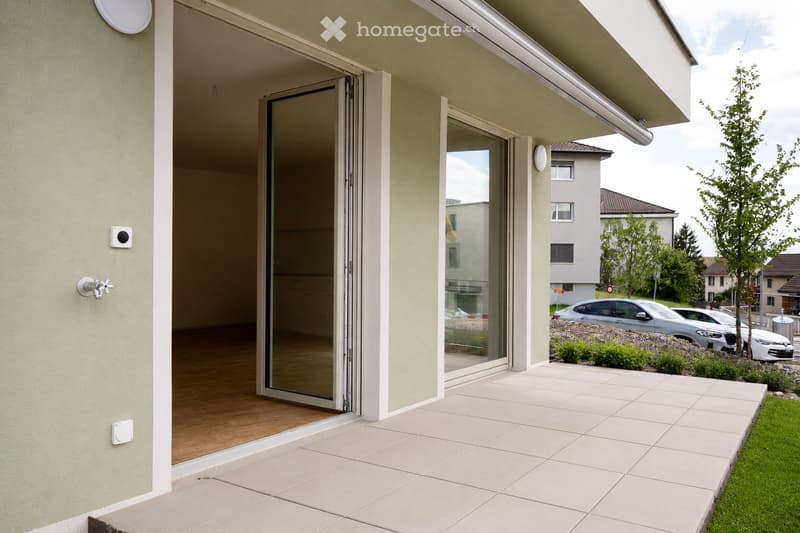 Balcony with large sliding glass doors, tiled floor, and a view of a residential area with parked cars and greenery.