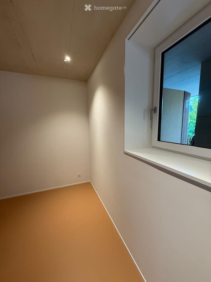 Empty room with beige walls, light brown floor, and a large window with a white sill. No furniture or equipment is present.