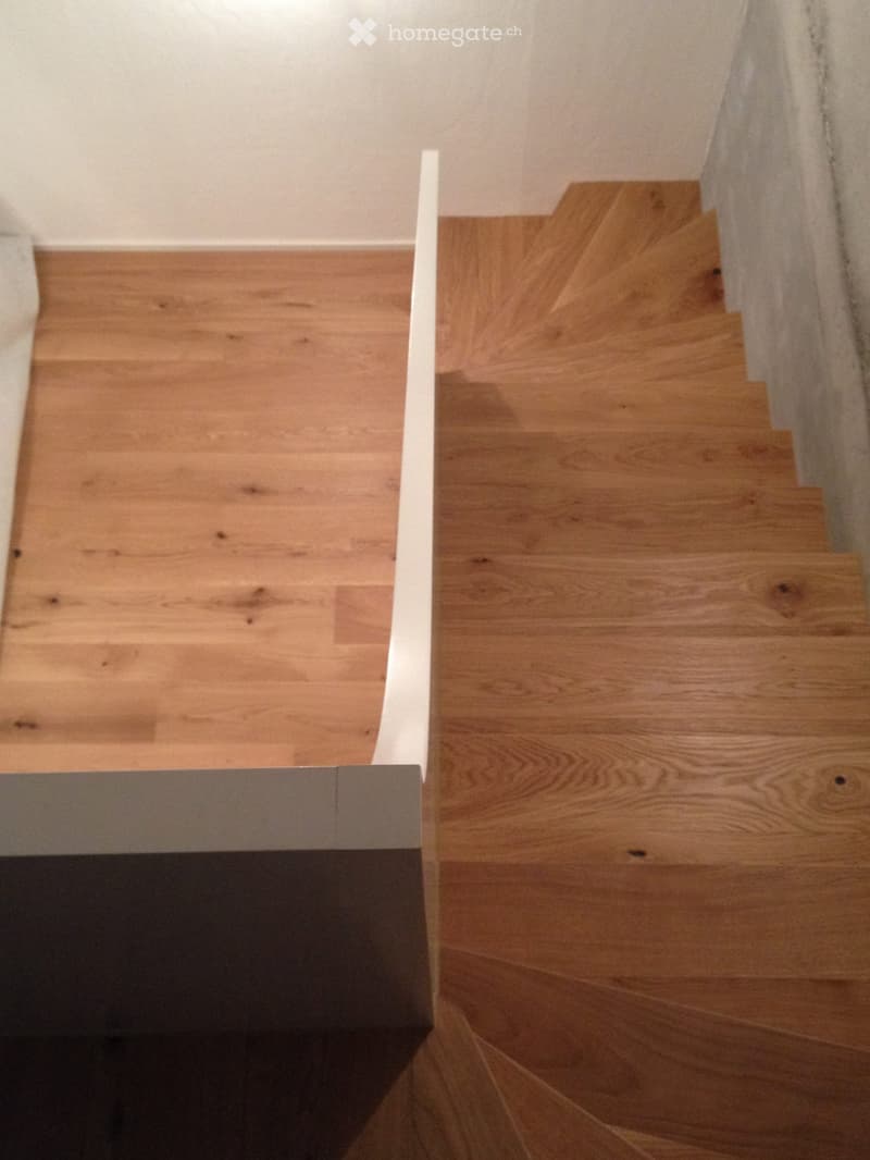 Wooden staircase with light-colored steps and a white handrail, leading upwards in a modern interior setting.