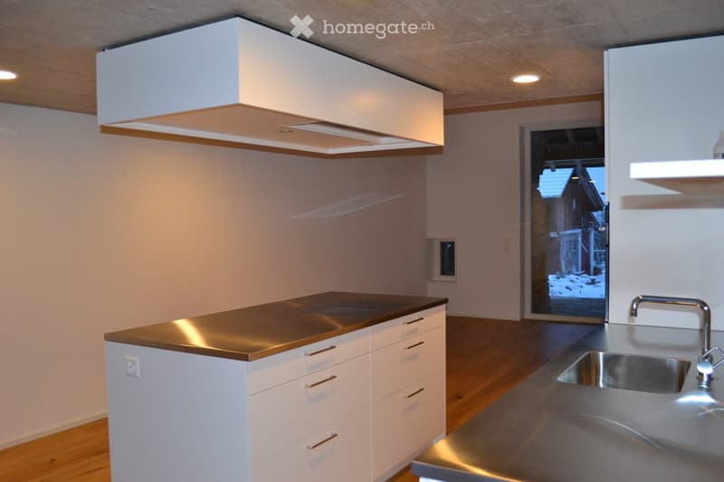 Modern kitchen with white cabinets, stainless steel sink, and a copper countertop. Features a large range hood and a view of a snowy outdoor scene through a glass door.