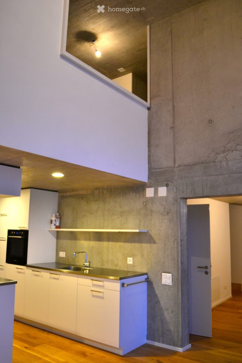 Modern kitchen with white cabinets, stainless steel sink, faucet, and oven. Concrete accent wall and wooden flooring.