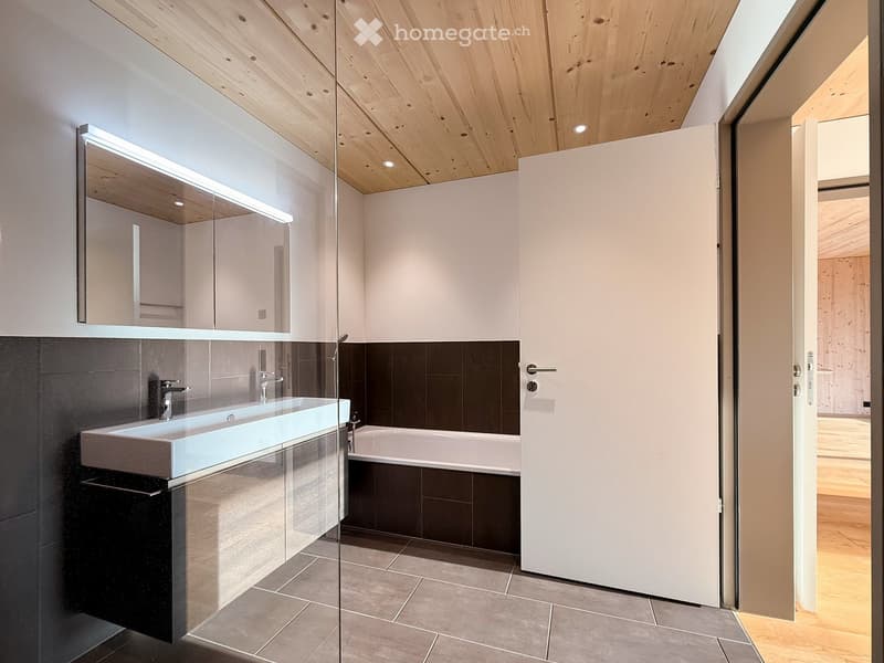 Modern bathroom with a sleek sink, bathtub, large mirror, and wooden ceiling.