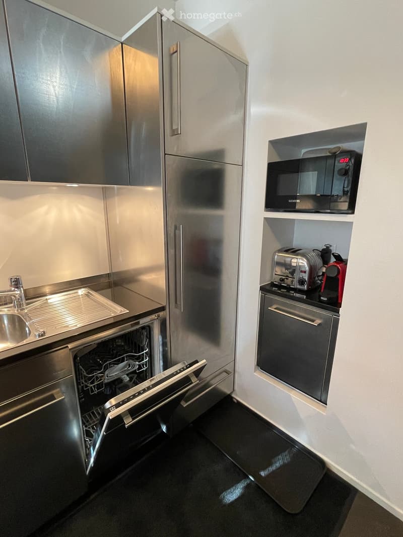 Modern kitchen with stainless steel appliances, including a dishwasher, microwave, toaster, and coffee maker, along with a sink and faucet.