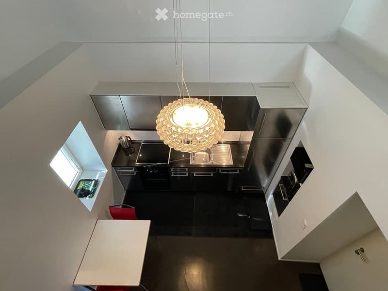 Modern kitchen with sleek black cabinets, a central island, a pendant light fixture, a small dining area with a table and chair, and a window with a view.