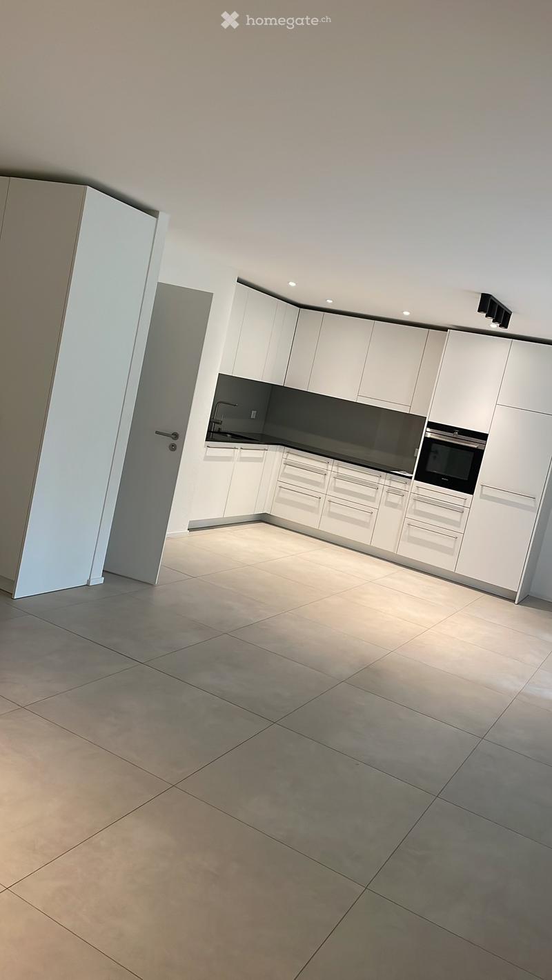 Empty kitchen with white cabinets, stainless steel sink, and built-in oven. The space features tiled flooring and recessed lighting.