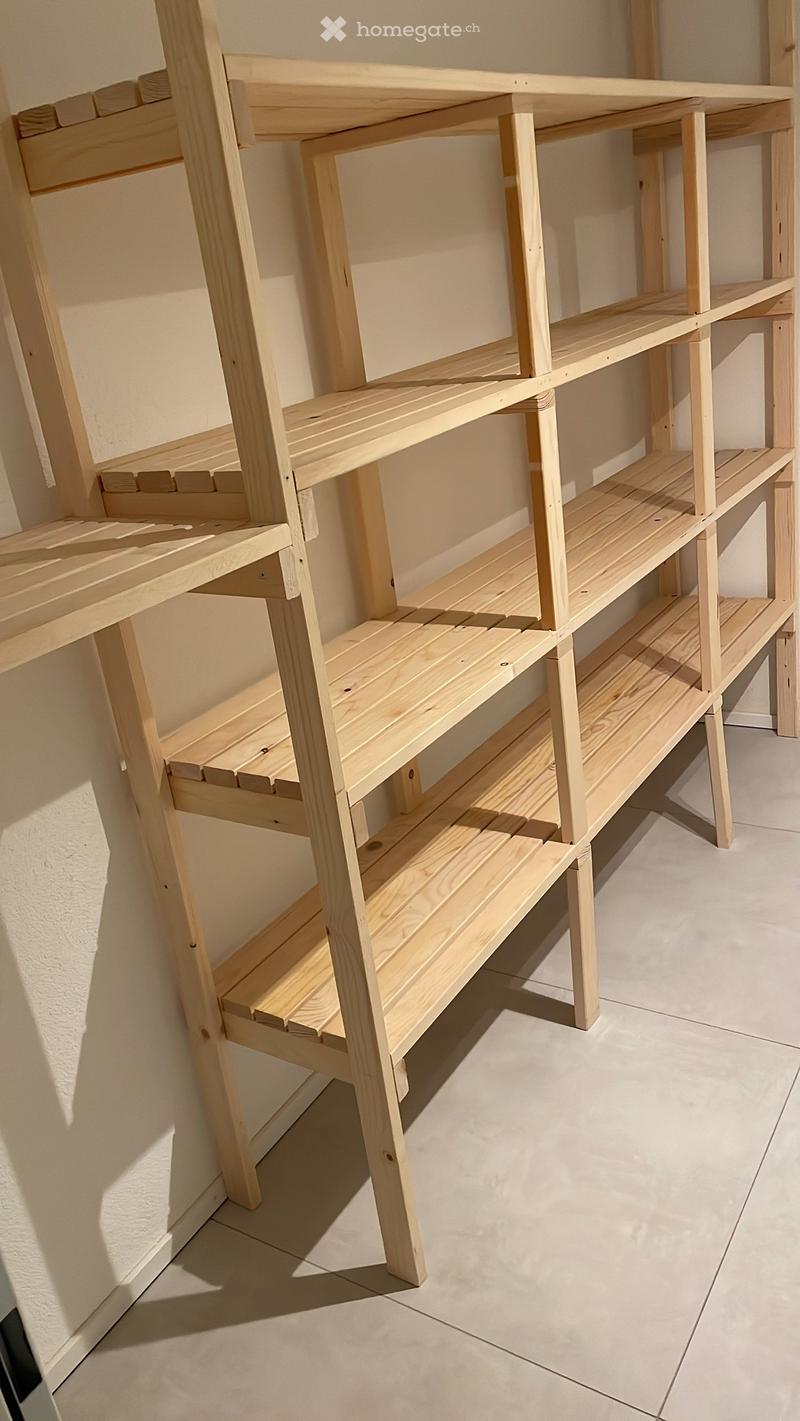 Empty room with a wooden shelving unit against the wall. The shelves are constructed from light-colored wood and are empty, with no items placed on them.