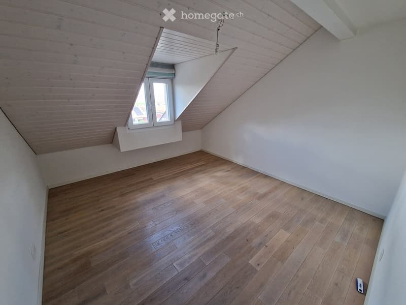 Empty attic room with wooden flooring, white walls, and a skylight window providing natural light.