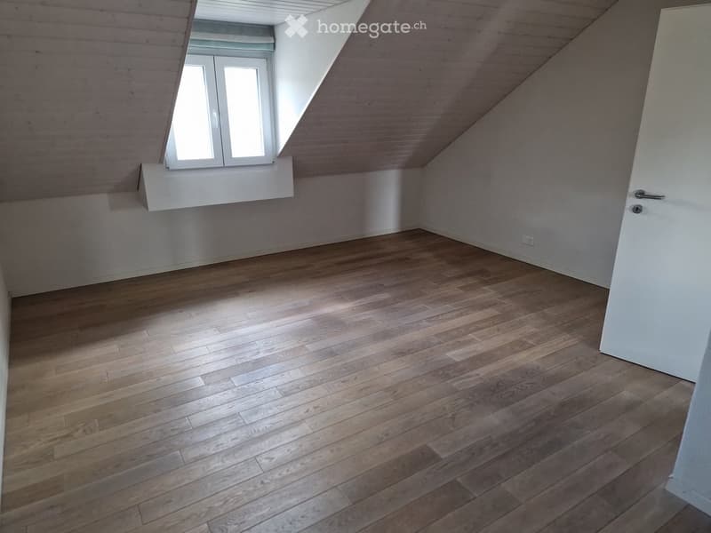 Empty attic room with wooden flooring, white walls, and a skylight window. No furniture or equipment present.