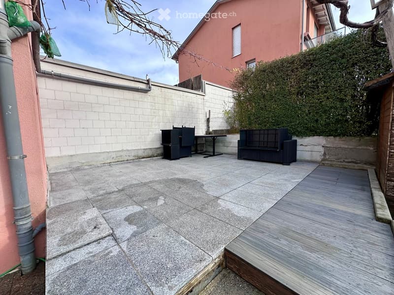 Outdoor seating area, tiled floor, wooden deck, stone walls, a building in the background