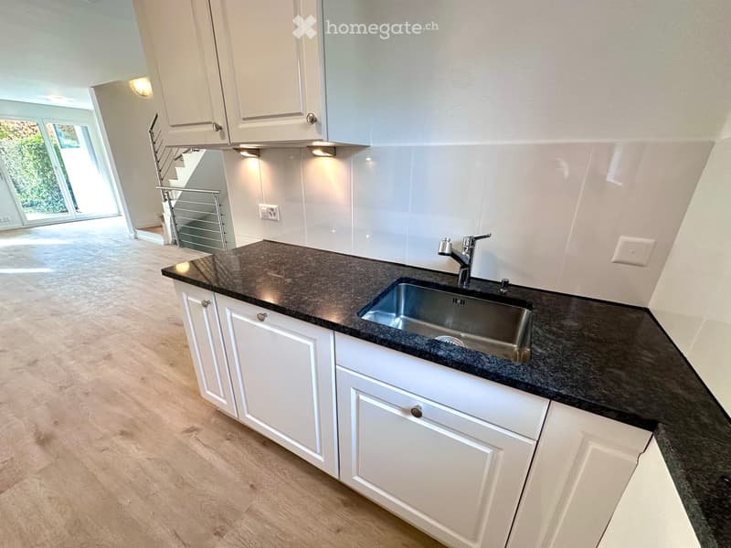 White cabinets, black countertops, stainless steel sink, chrome faucet, light wooden floor, glass door, no appliances