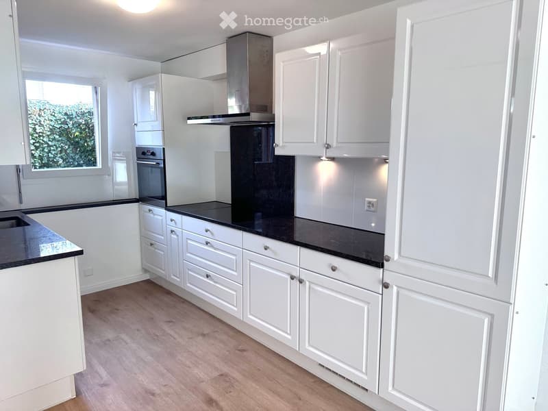 Modern kitchen with white cabinets, black marble countertops, stainless steel appliances, wooden floor, window, extractor hood, power outlet, and built-in dishwasher.