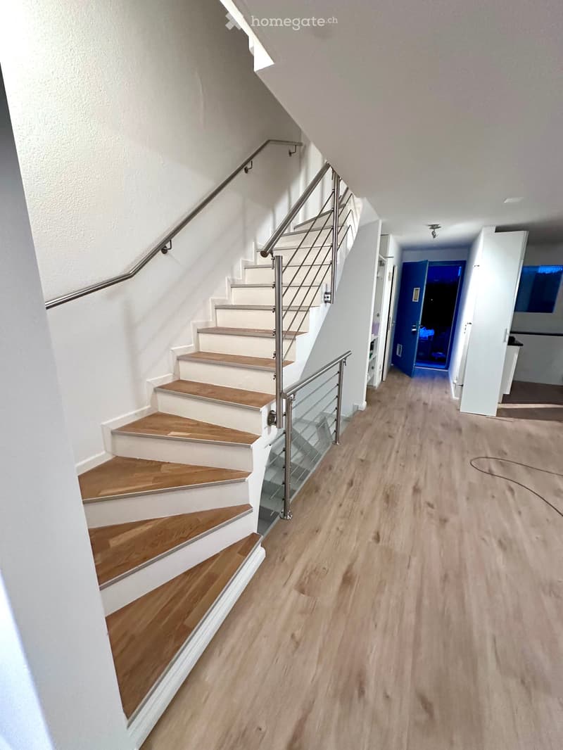 Wooden stairs, light hardwood floors, metal railings, open layout.