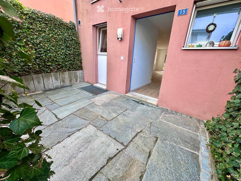 paved entrance with plants on both sides, pink exterior with windows, open door