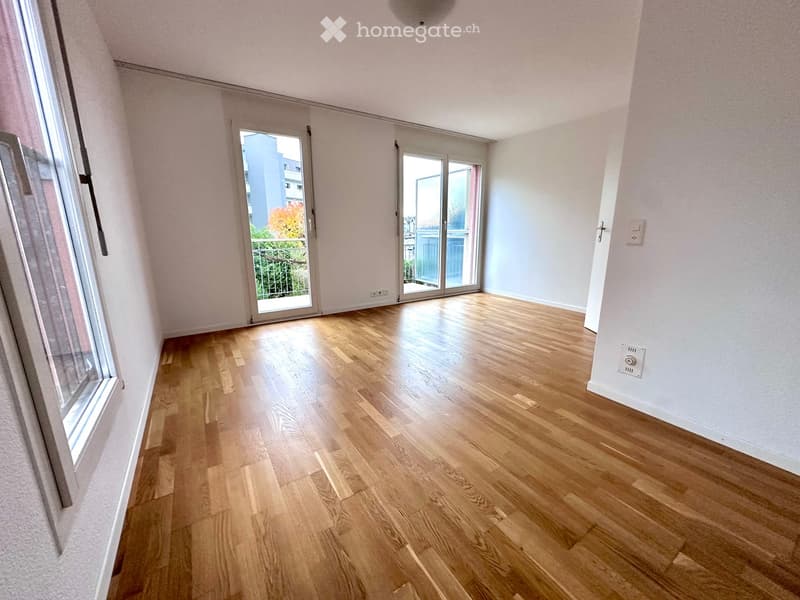Empty room, hardwood floors, glass sliding doors leading to a balcony, white walls, overhead light, electrical outlets.