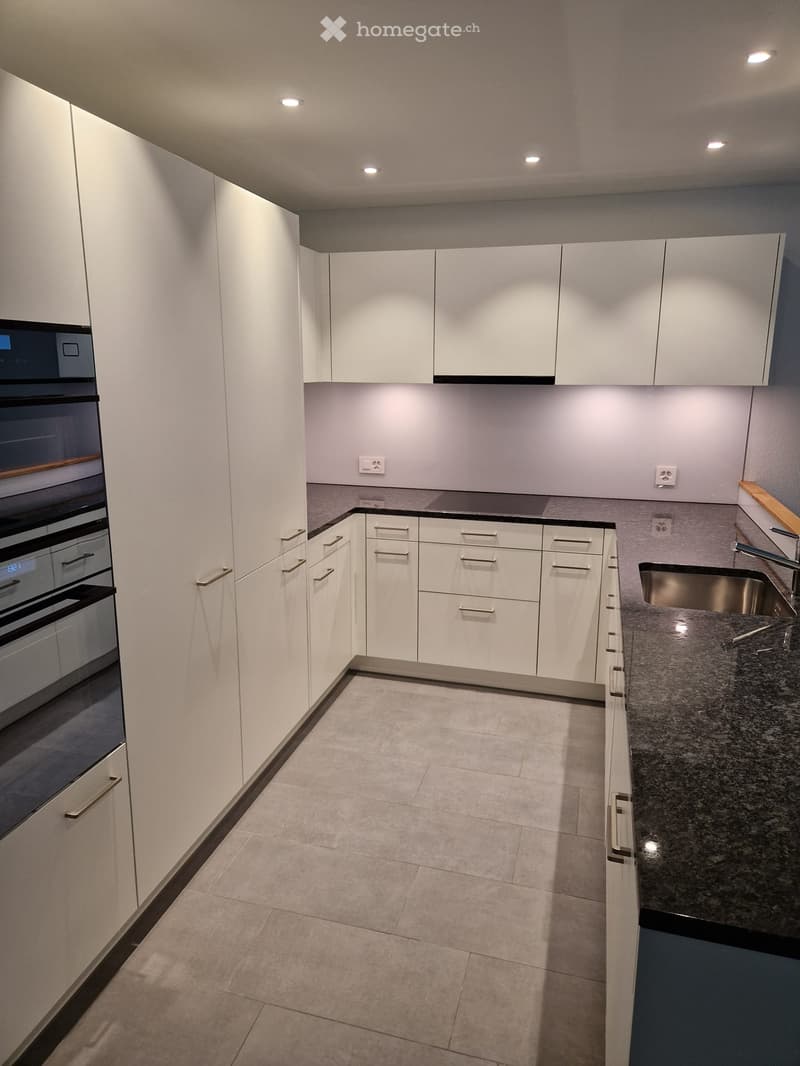 Modern kitchen with white cabinets, granite countertop, stainless steel sink, and built-in oven.