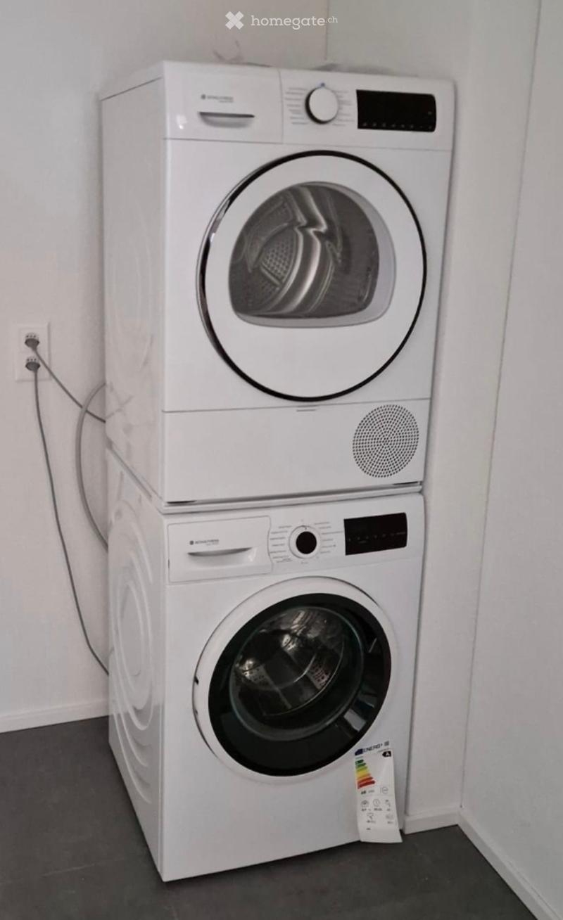 A compact, modern bathroom featuring a stacked washing machine and dryer unit. The appliances are white with sleek, contemporary designs and digital control panels.