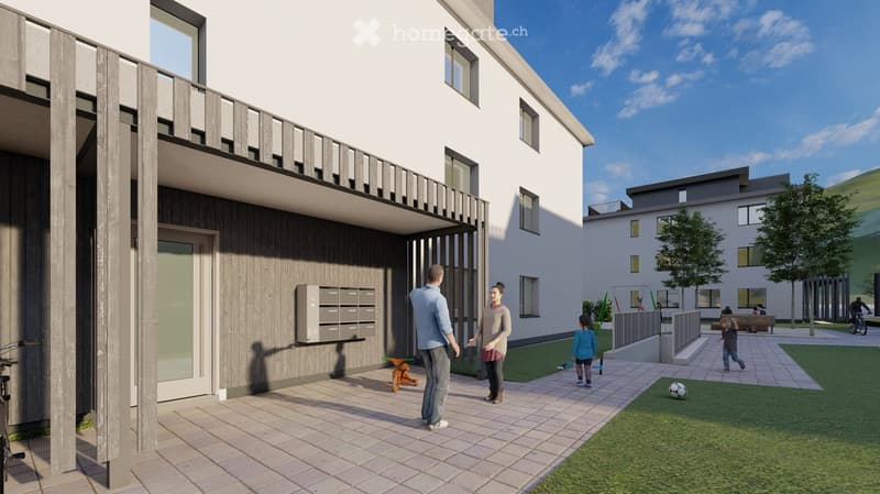 Modern two-story residential building with a balcony, mailboxes, and a paved entrance area. The surrounding area includes a grassy lawn, playground equipment, and a small soccer field.