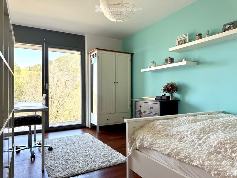 Bright bedroom with a white bed, fluffy white throw, white rug, desk with chair, white cabinet, and shelves with decorative items.