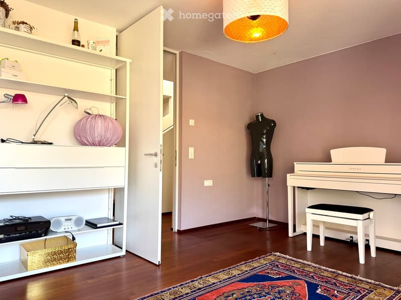 A well-furnished room with a white piano, a matching stool, a decorative balloon, a mannequin, a shelf with various items including a printer, radio, and decorative objects, and a hanging lamp with an orange shade.