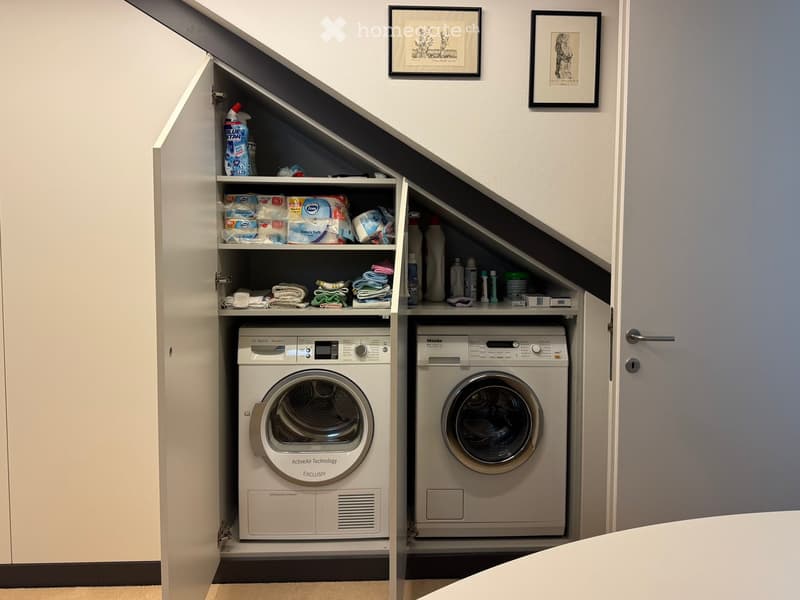Compact laundry area with Bosch and Miele washing machines, built-in cabinets, and neatly stored towels and cleaning supplies.