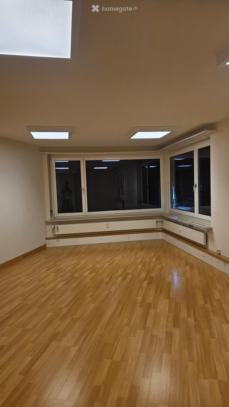 Empty room with wooden flooring, large windows, and recessed ceiling lights.