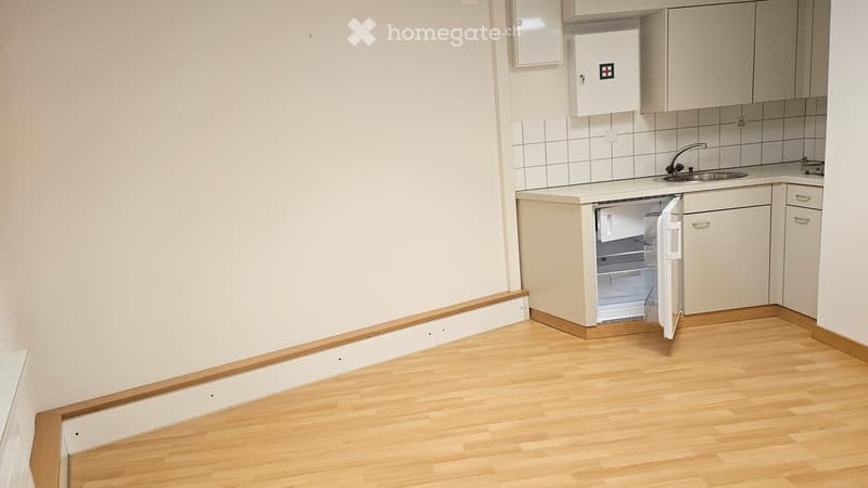 Compact kitchen with light wooden flooring, white cabinets, a small refrigerator, and a sink.