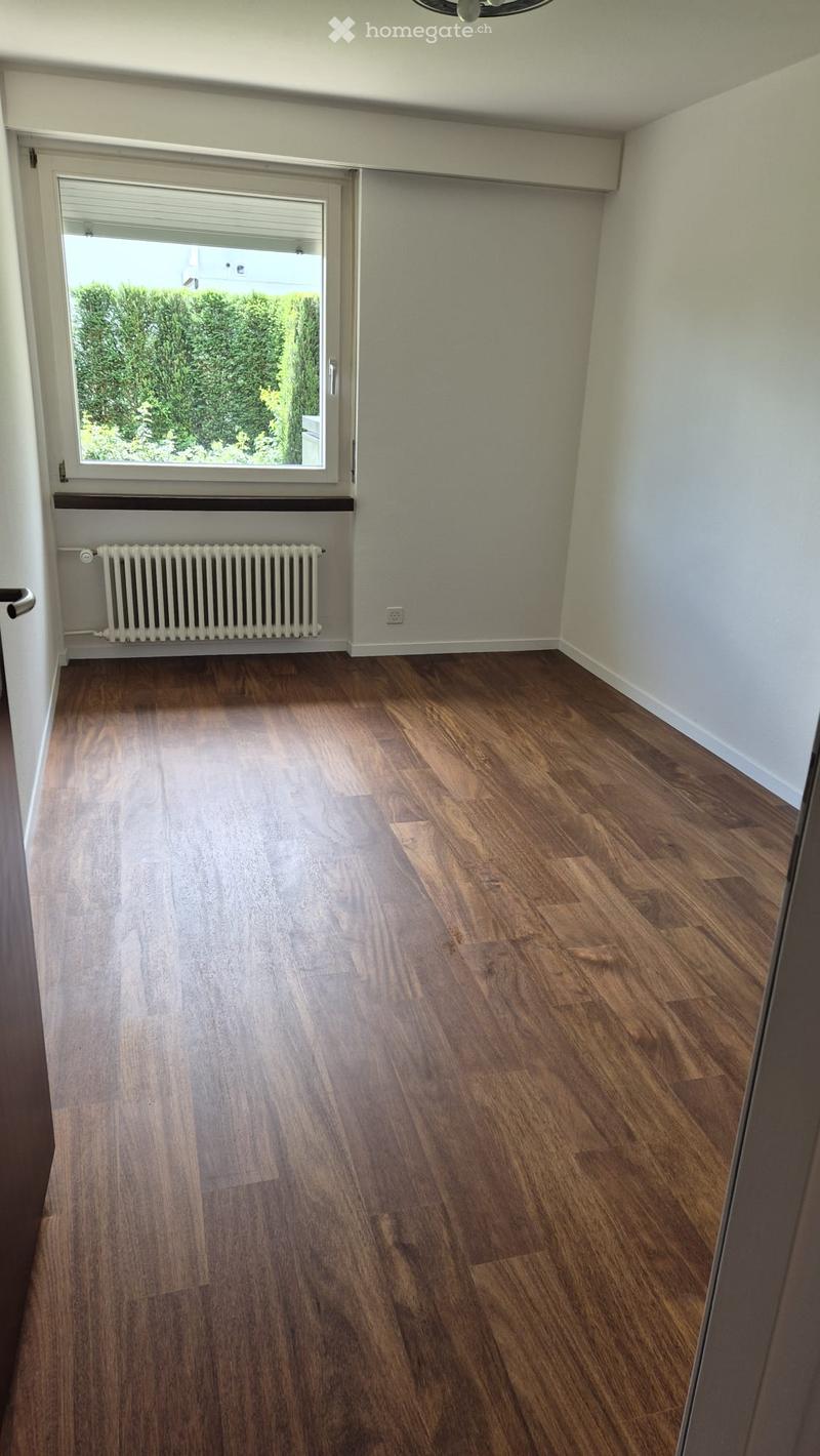 Empty room with wooden flooring, white walls, a window with blinds, and a radiator below the window.